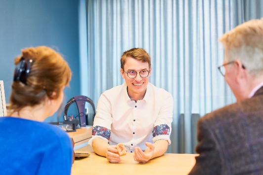 Junger Berater im Gespräch mit älterem Paar bei Finanzberatung im modernen Büro.