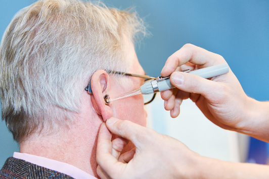 Ein Hörakustiker passt einem Senior ein modernes Hörgerät im Ohr präzise an.